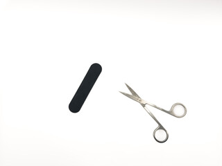 A pair of scissors and a nail file are on a white background. The scissors are silver and the nail file is black