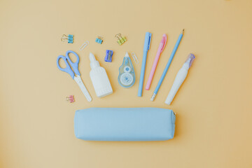 Assortment of pastel school supplies laid out with a pencil case on a light peach background.