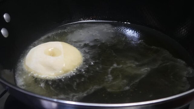 The process of frying donuts in a pan filled with hot oil. Some of the dough is still white and half cooked, while others have begun to turn brown. Making homemade donuts