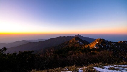 Panoramic sunset view of a mountain range, showing layers of peaks and valleys, with a hint of snow near the foreground