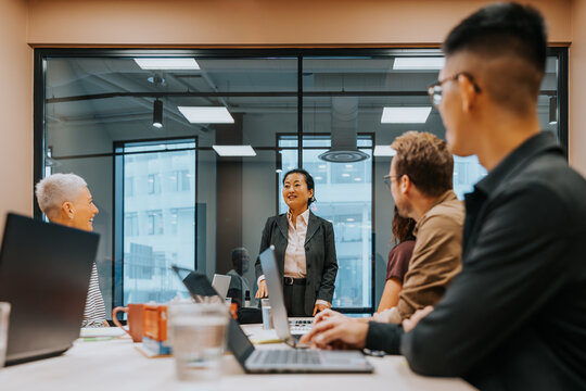 Mature businesswoman discussing strategies with colleagues while standing in meeting room at office