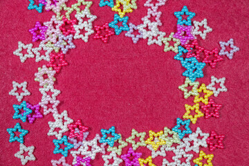 Colorful star beads arranged in a circular frame on red fabric background