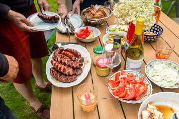 party w ogrodzie, kiełbaski z grilla, sałatki wino i dodatki na drewnianym stole