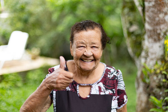 Smiling elderly woman showing thumbs up outdoors. Concept of active aging, happiness, and positivity in rural lifestyle. Natural background and authentic expression.