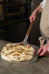 Male chef in beige apron skillfully preparing a delicious pizza topped with chicken and cheese, showcasing culinary expertise in a professional kitchen environment