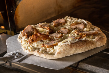 Freshly baked pizza topped with grilled chicken, onions, and herbs, resting on a metal pizza peel,...