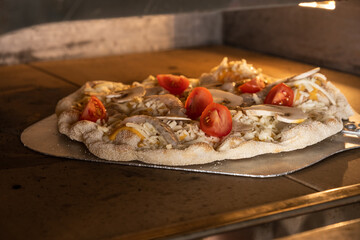 Freshly prepared pizza with sliced tomatoes and onions is baking in a traditional oven, showcasing...