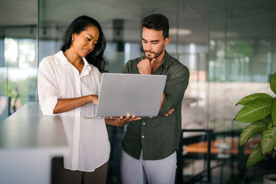 Multiracial colleagues discussing startup project and smiling during workday in office interior