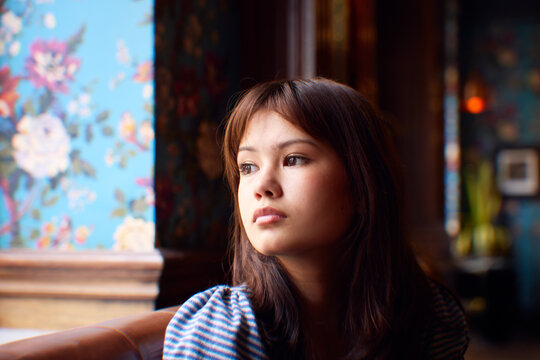 Thoughtful teenage girl looking away while sitting on sofa
