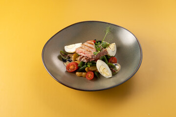 Gourmet dish featuring grilled salmon fillet, fresh vegetables, and garnishes served in a stylish bowl against a vibrant yellow background, showcasing culinary artistry and presentation