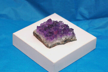 Purple amethyst cluster cristals on a white  platform  against deep blue background. Closeup photo...
