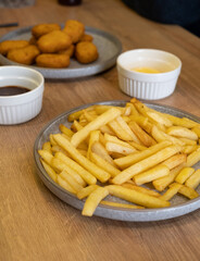 Crispy golden French fries served on a gray plate, accompanied by chicken nuggets and dipping sauces, creating a delicious fast food meal experience