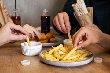 Group of diverse hands reaching for crispy golden fries on a plate, accompanied by dipping sauces, creating a lively and inviting dining atmosphere with shared enjoyment
