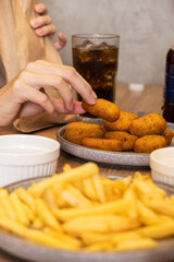 Hand reaching for crispy golden snacks on a plate, with a side of fries and a refreshing drink, creating a casual dining atmosphere with delicious food