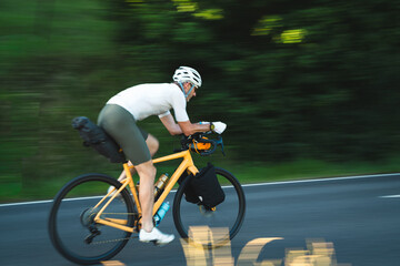 Radfahrer fährt auf gelben Fahrrad und Gepäck auf der Strasse in den Sonnenuntergang, bikpacking, Radreise