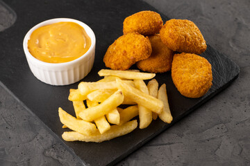 Golden crispy chicken nuggets served with golden fries and creamy dipping sauce on a black slate plate, showcasing delicious fast food indulgence and culinary delight