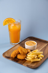 Delicious golden chicken nuggets served with crispy fries and a refreshing orange drink on a wooden platter against a soft blue background, perfect for casual dining moments