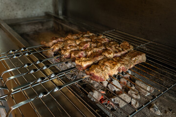 Grilled meat skewers cooking over hot coals on a barbecue grill, showcasing delicious barbecue preparation with smoke rising and a rustic kitchen atmosphere