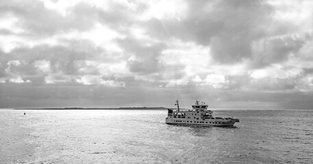Car ferry with vacationers traveling from Norddeich Mole to Norderney (Germany) on the crossing through the Wadden Sea World Heritage. Atmospheric black-and-white photograph in the evening light.