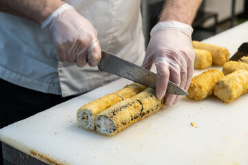 Chef with gloved hands skillfully slicing sushi rolls on a cutting board, showcasing culinary expertise and precision in food preparation and presentation techniques