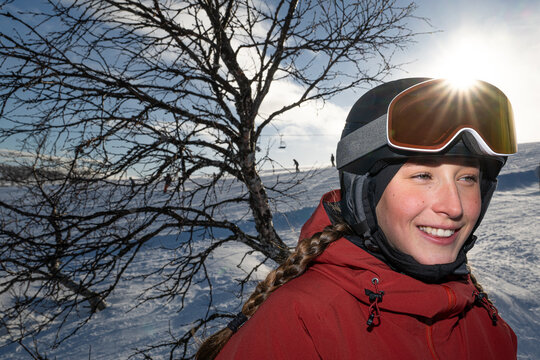 Smiling teenage girl wearing skiing helmet and googles near tree at sunny day