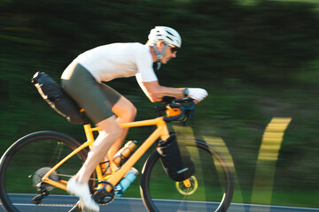 Radfahrer fährt auf gelben Fahrrad und Gepäck auf der Strasse in den Sonnenuntergang, bikpacking, Radreise