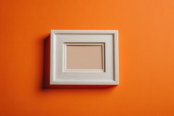 An overhead view of a plain small picture frame against an orange backdrop