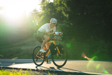 Radfahrer fährt auf gelben Fahrrad und Gepäck auf der Strasse in den Sonnenuntergang, bikpacking, Radreise