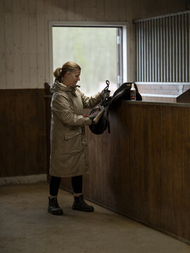 Full length of female rancher cleaning horse saddle in stable