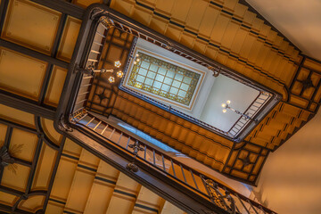 Decorative staircase viewed from below. Skylight with stained glass crowns the perspective.