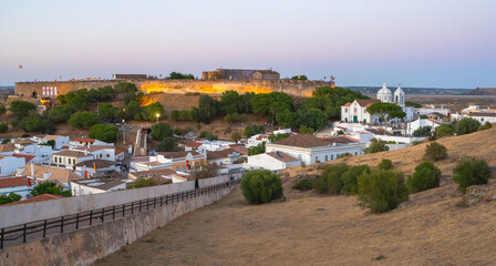 The historic walls of Castro Marim fortress shine with golden light as visitors stroll the upper castle grounds at twilight.