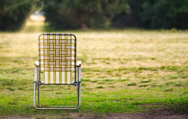 Empty folding chair standing on grass in nature setting during sunset
