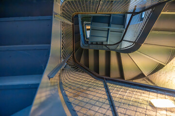 An industrial metal staircase spirals upward with repeating shapes. The railing s mesh design adds...