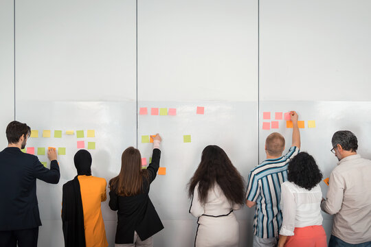 Rear view of male and female business professionals sticking adhesive notes on whiteboard in office board room