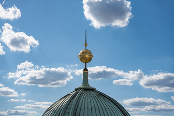 The golden spire of the cathedral's dome rises into the clear sky. White clouds enhance the depth...