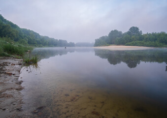 A calm lake with a cloudy sky in the background. The sky is blue and the trees are green