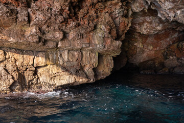 A scenic view of a rocky coastal cave entrance with clear blue water