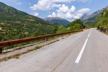 A tranquil mountain road with a railing overlooks lush forested hills