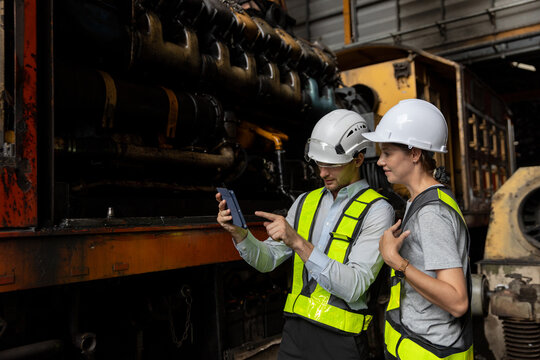 Two engineer wearing safety gear walking through a railway maintenance, inspecting train parts and infrastructure. Concept of industrial safety, rail engineering and station inspection.