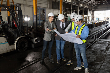 Fototapeta premium Group of railway engineers and business professionals in safety hard hat reviewing blueprint plans inside an industrial factory. Concept of project planning brainstorming, engineering teamwork.