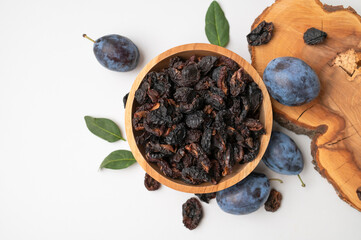 Dried plum prunes in wooden bowl on light gray background flat lay top view. Dried fruit, sweet tasty healthy pitted natural dessert, close-up. Food background