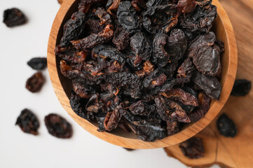 Dried plum prunes in wooden bowl on light gray background flat lay top view. Dried fruit, sweet tasty healthy pitted natural dessert, close-up. Food background