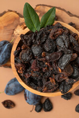 Dried plum prunes in wooden bowl, fresh plums with green leaves on brown background flat lay top view. Dried fruit, sweet tasty healthy pitted natural dessert. Food background