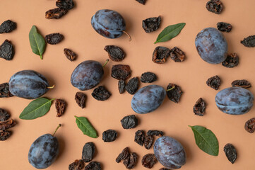 Dried plum prunes and fresh plums with green leaves on brown background flat lay top view. Food background, dried delicious fruits, sweet healthy dessert, healthy eating