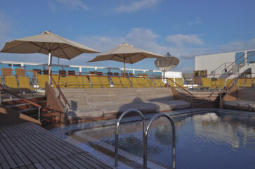 Pooldeck or swimmingpool with sun deck on modern cruiseship or cruise ship liner with elegant lounge furniture deck chairs and rattan sun beds loungers