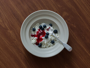 Delicious healthy breakfast - cottage cheese with Greek yogurt, raspberry sauce and blueberries on a wooden background, top view