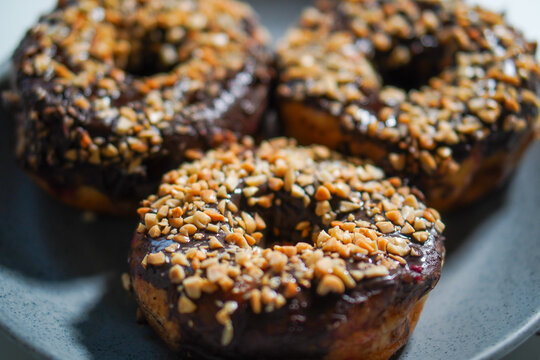 three chocolate donuts with peanut topping on a plate