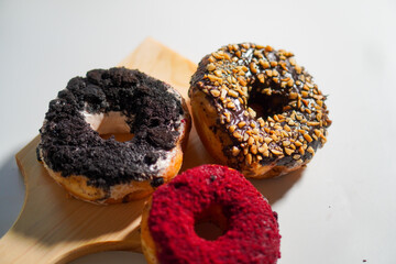 Three donuts with different flavors and toppings on a wooden stand