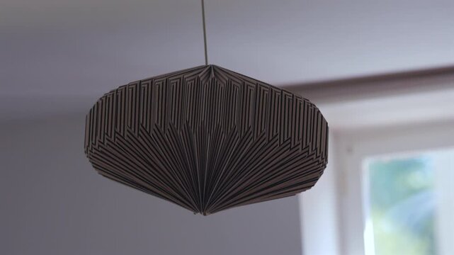 Close-up of modern geometric pendant lamp hanging from ceiling in minimalist home interior with soft natural daylight