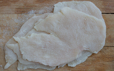 Chicken slices breaded with flour on a wooden cutting board